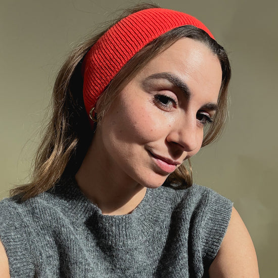 eine frau schaut in die kamera und trägt ein stirnband aus merinowolle in der farbe rot/orange