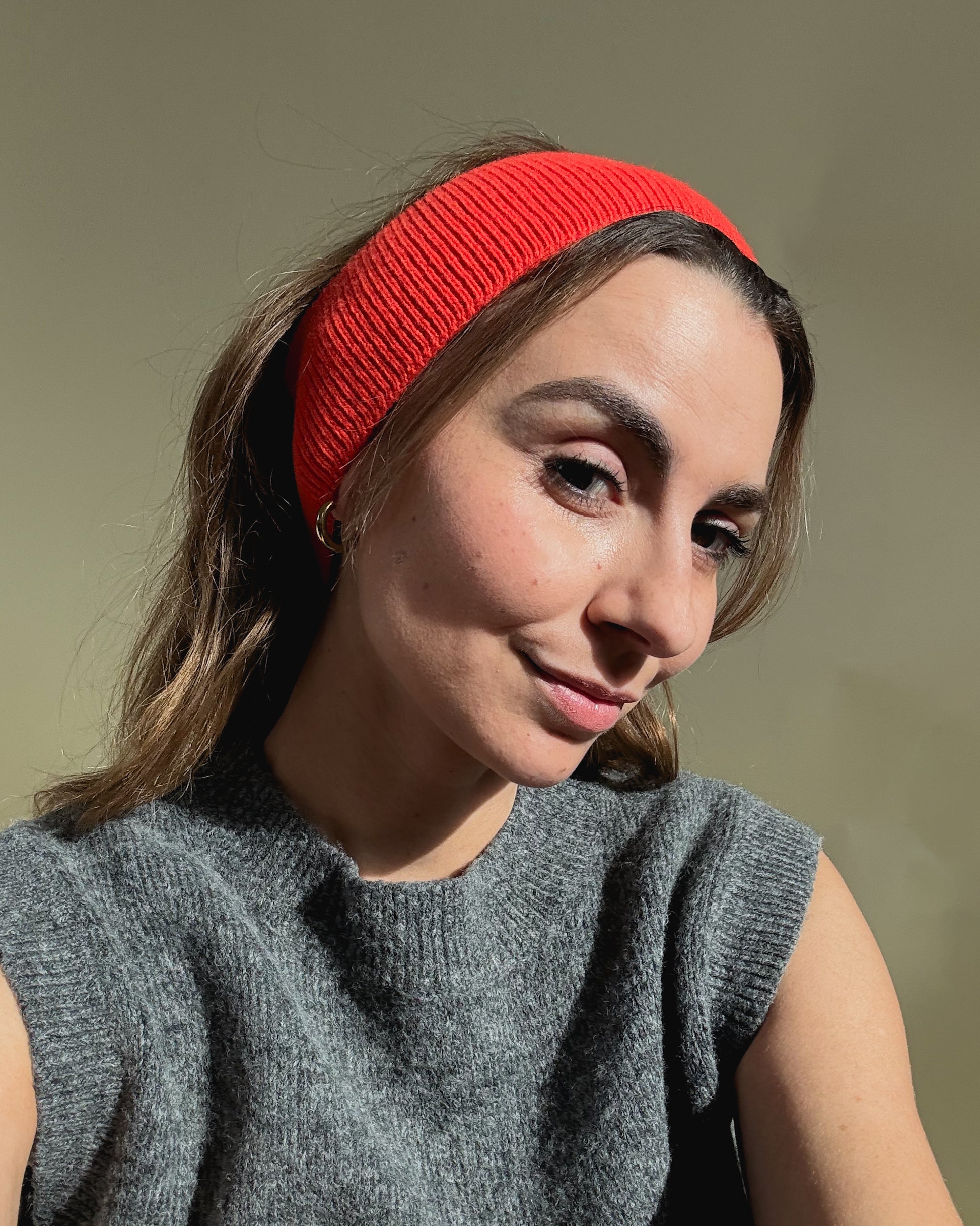 eine frau schaut in die kamera und trägt ein stirnband aus merinowolle in der farbe rot/orange