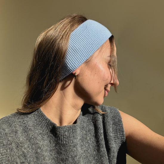 eine frau schaut in die kamera und trägt ein stirnband aus merinowolle in der farbe blau