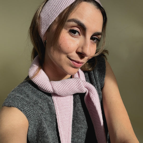 eine frau schaut in die kamera und trägt ein stirnband sowie einen mini scarf aus merinowolle in der farbe pink