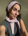 eine frau schaut in die kamera und trägt ein stirnband sowie einen mini scarf aus merinowolle in der farbe pink