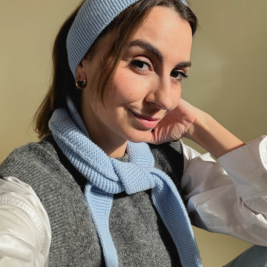 eine frau schaut in die kamera und trägt ein haarband sowie einen mini scarf aus merinowolle in der farbe hellblau