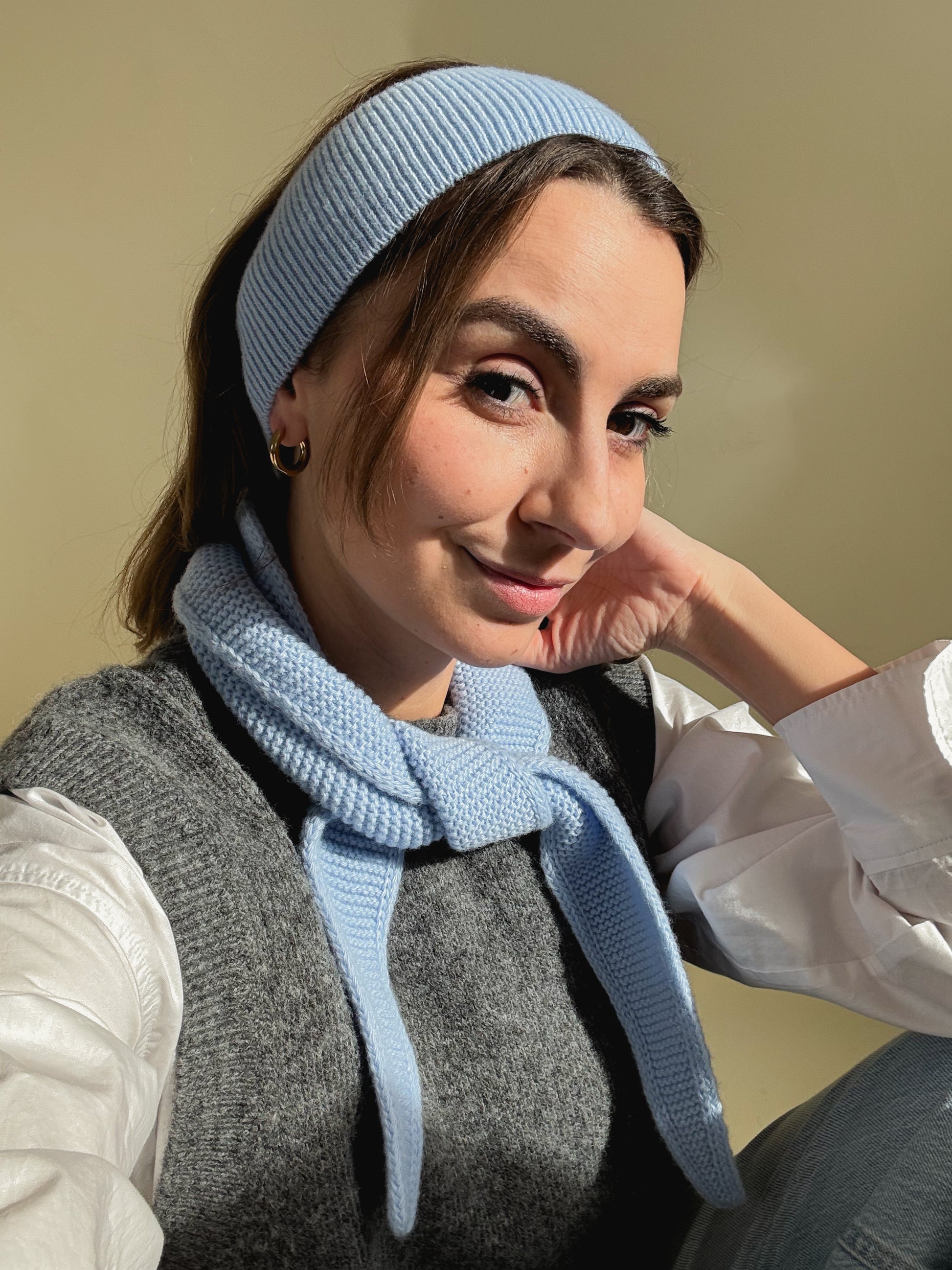eine frau schaut in die kamera und trägt ein haarband sowie einen mini scarf aus merinowolle in der farbe hellblau