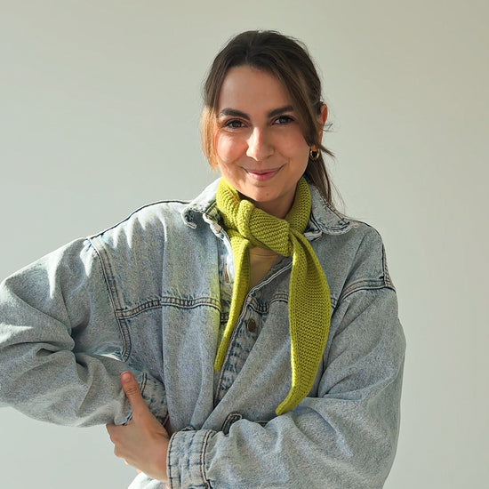 eine frau schaut in die kamera und trägt einen mini schal aus merinowolle in der farbe grün