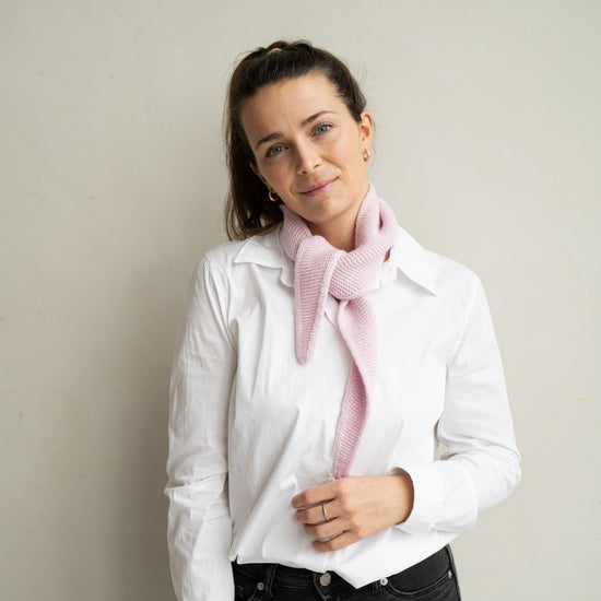 eine frau schaut zur seite und trägt einen mini schal aus merinowolle in der farbe pink