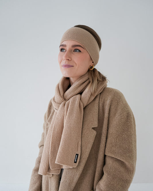 eine frau trägt einen schal und ein stirnband aus merinowolle in beige