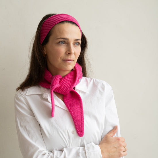 eine frau schaut zur seite und trägt einen mini schal und ein haarband aus merinowolle in der farbe pink