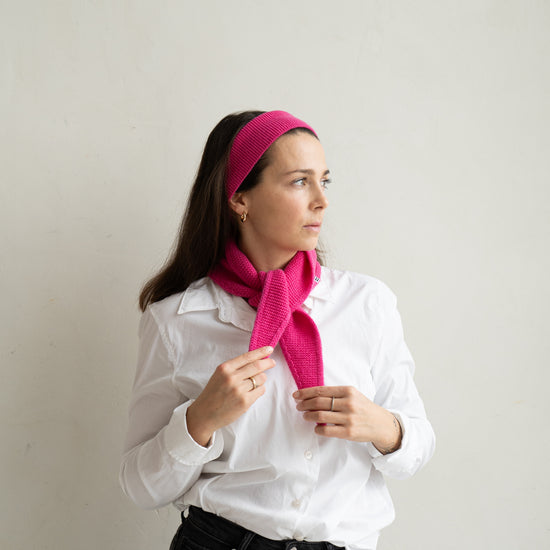 eine frau schaut zur seite und trägt einen mini schal und ein haarband aus merinowolle in der farbe pink