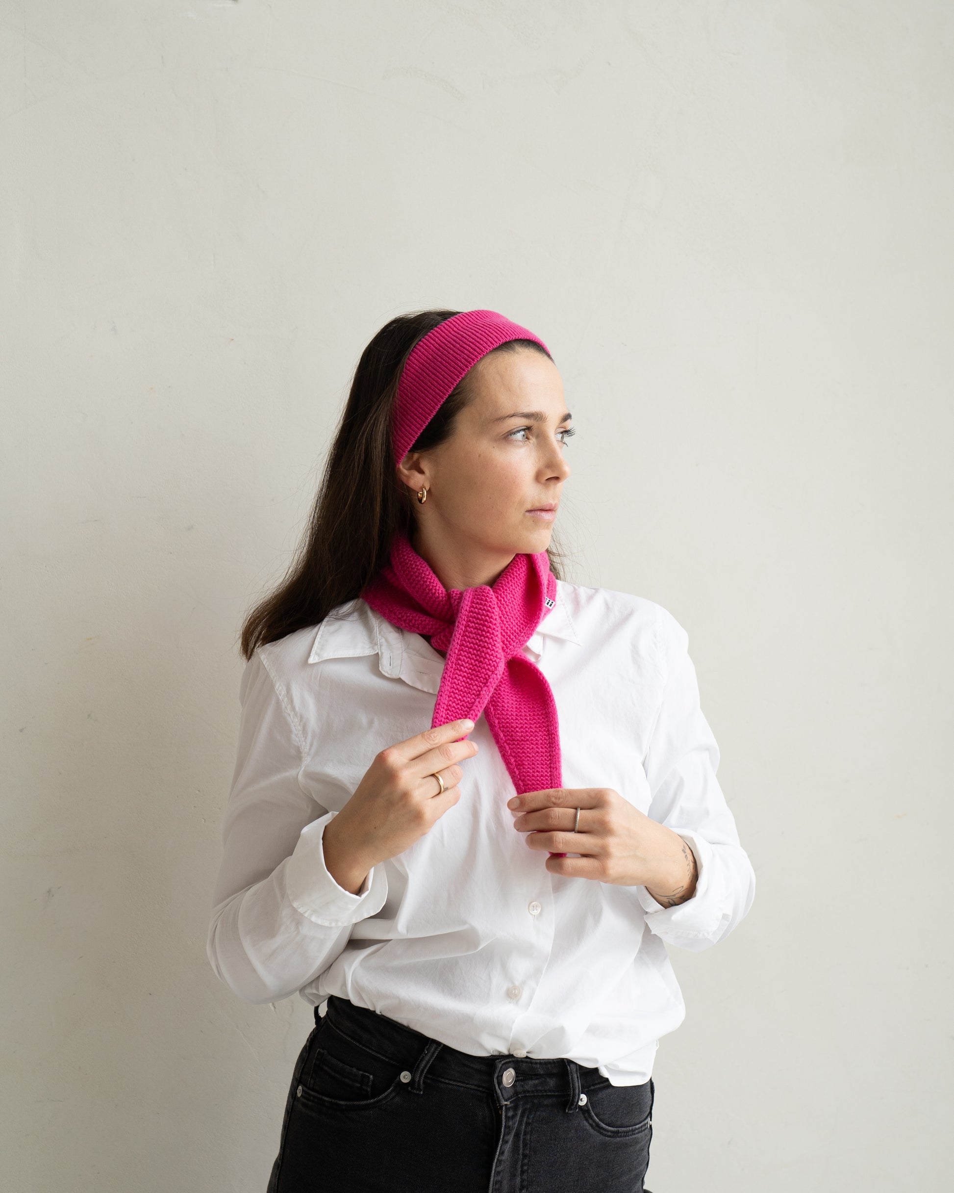 eine frau schaut zur seite und trägt einen mini schal und ein haarband aus merinowolle in der farbe pink